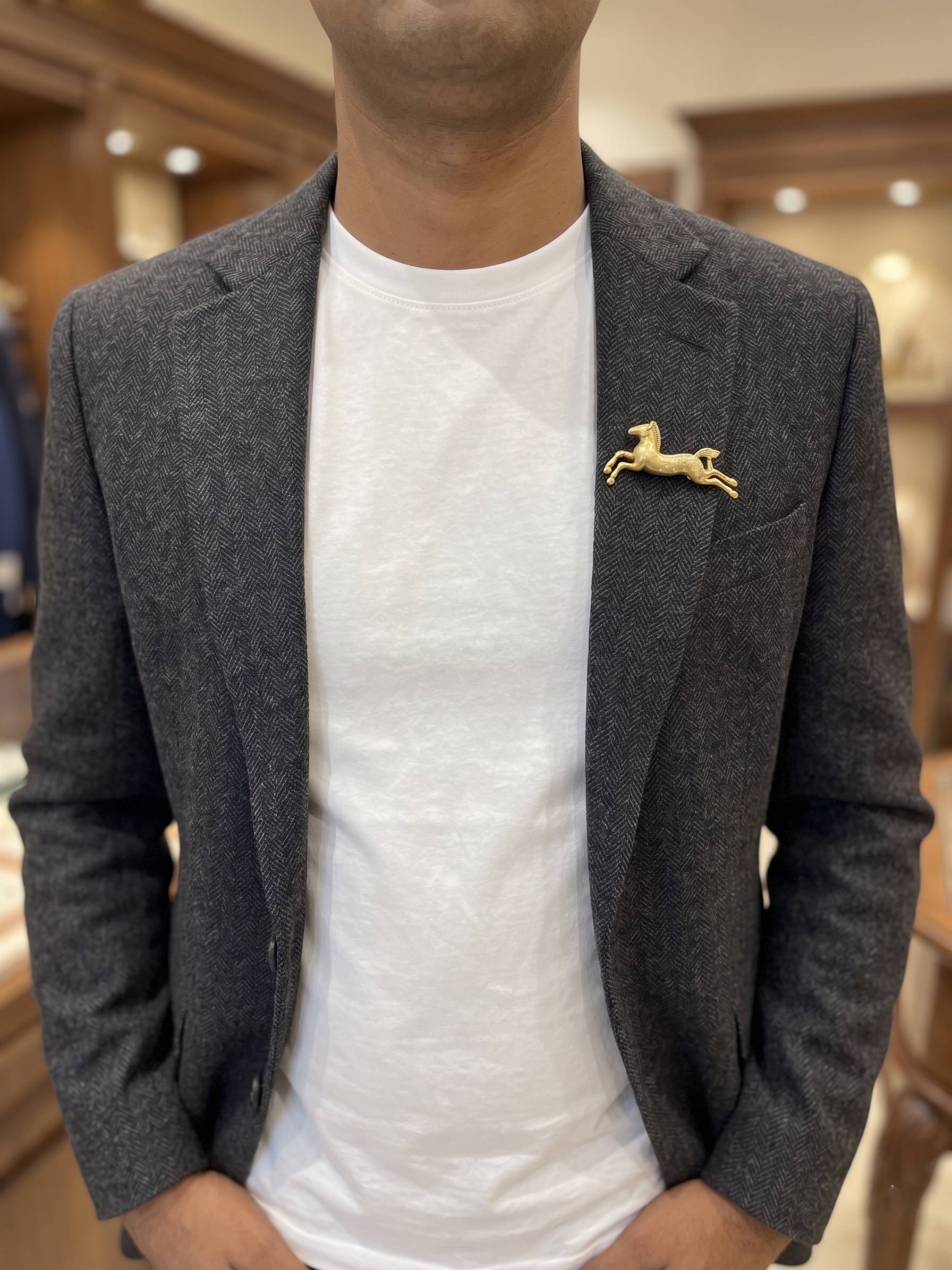 Person wearing a gray blazer with a gold brooch over a white shirt in an indoor setting.