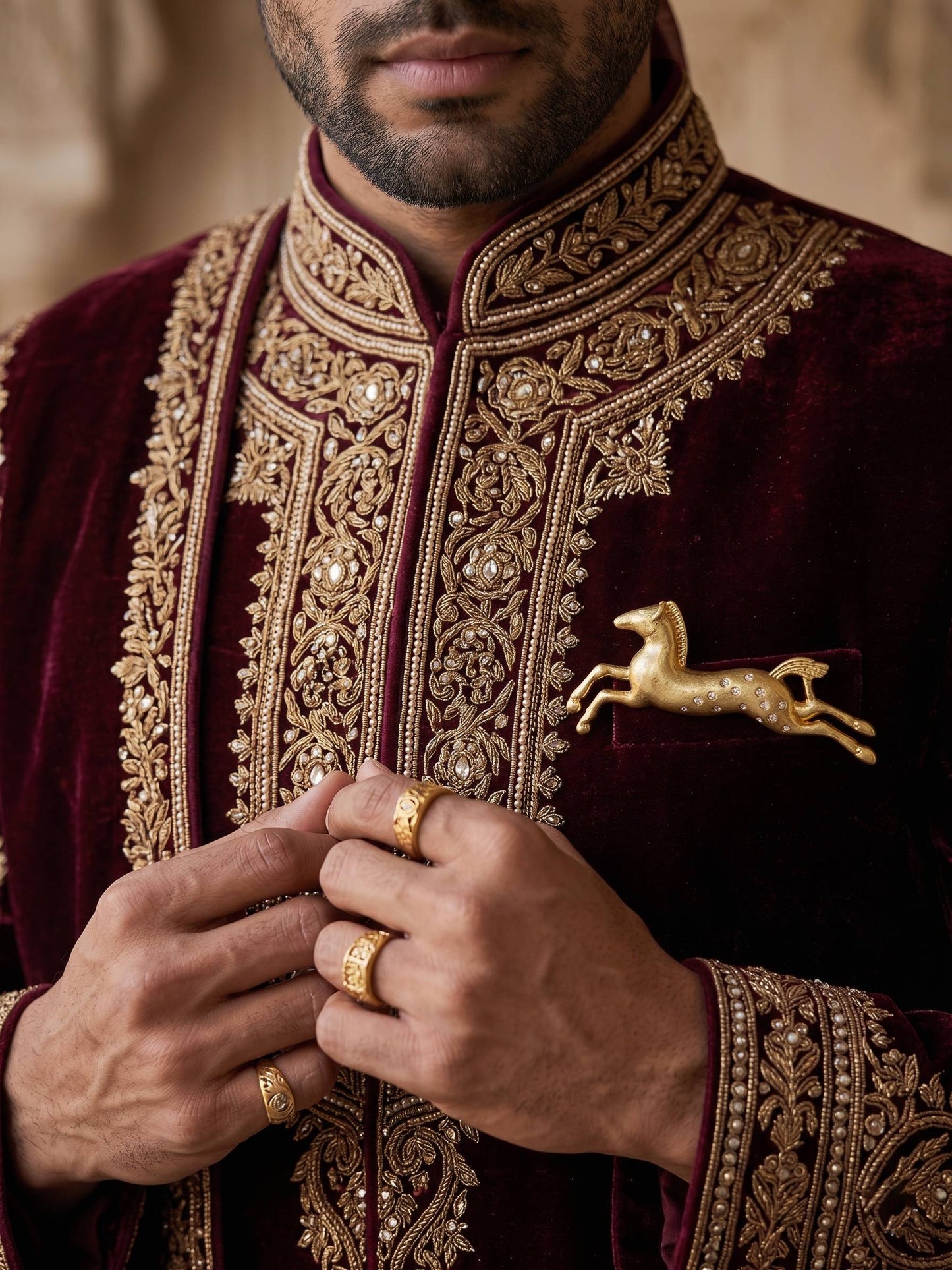 Man wearing a traditional embroidered outfit with gold detailing and a brooch.