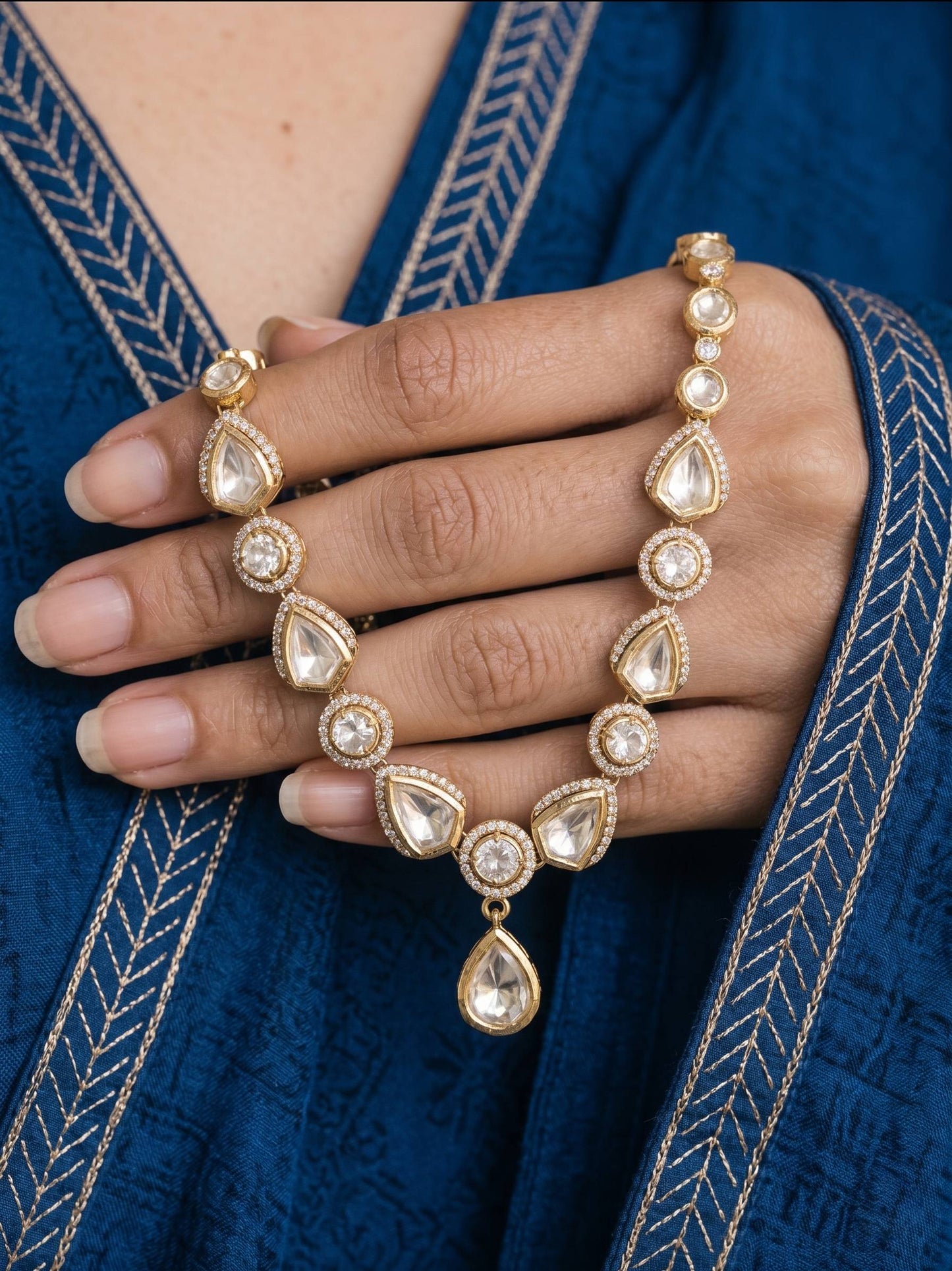 Hand wearing a gold bracelet and ring on a blue fabric background