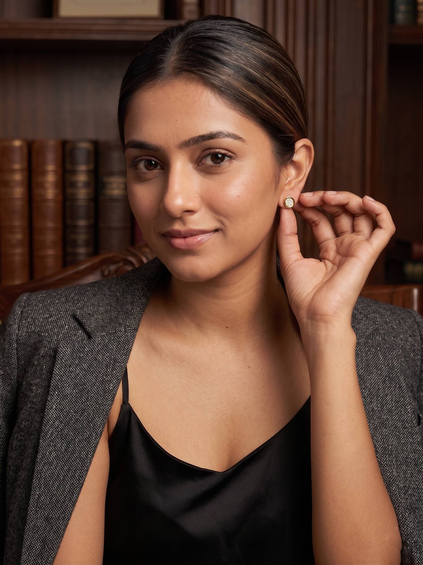Woman adjusting an earring in a professional setting with books in the background