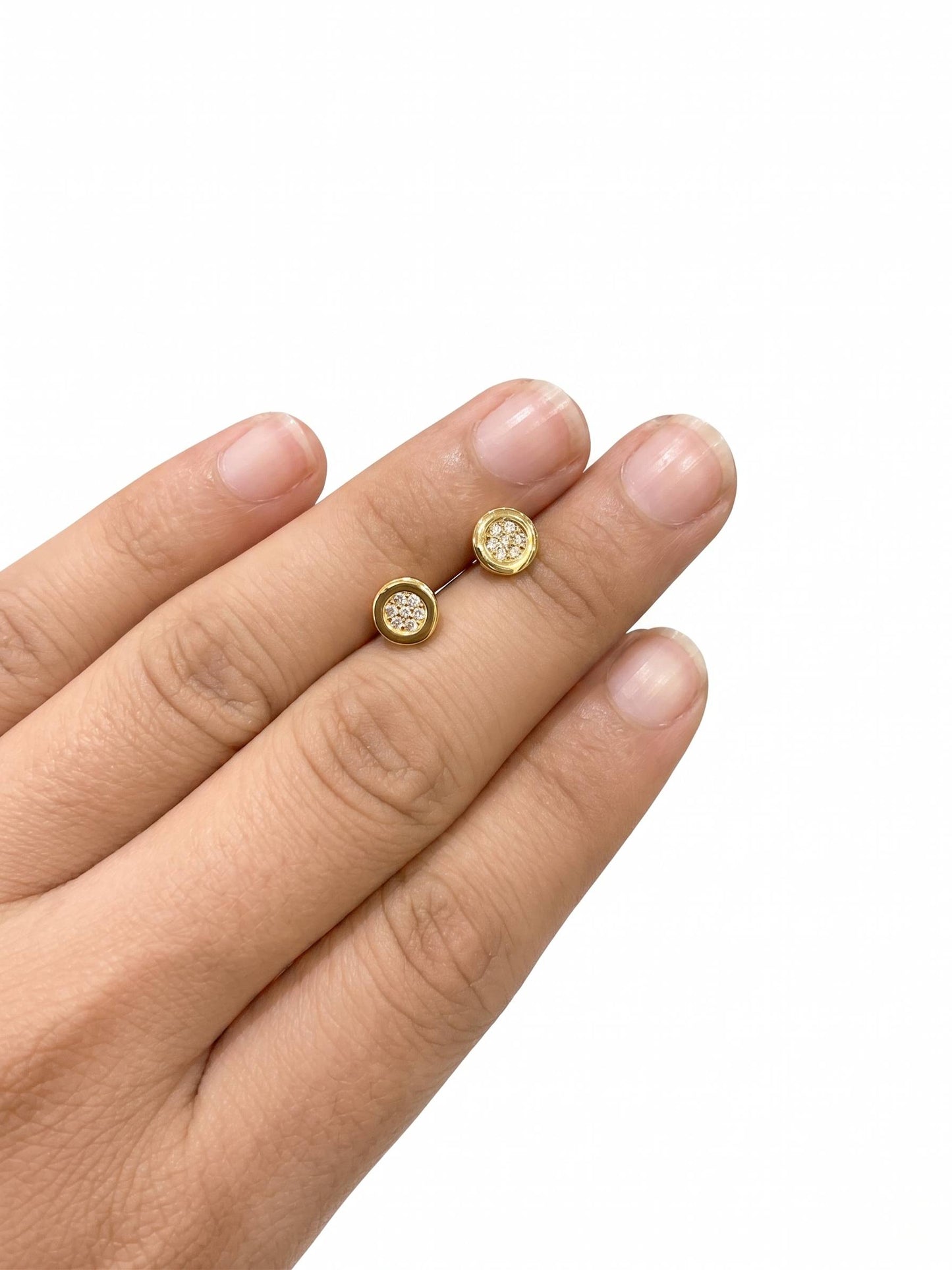 Gold stud earrings on a hand against a white background