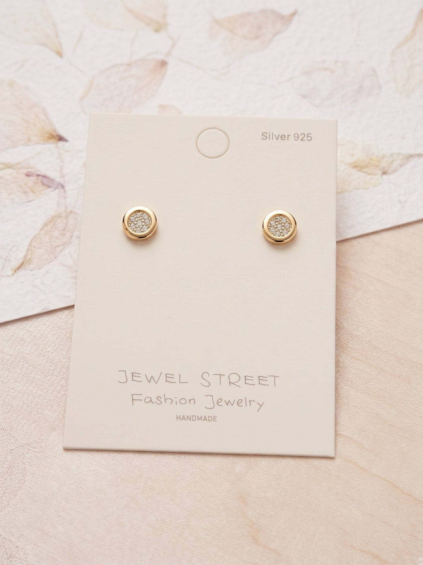 Gold earrings on a Jewel Street branded card with a floral background