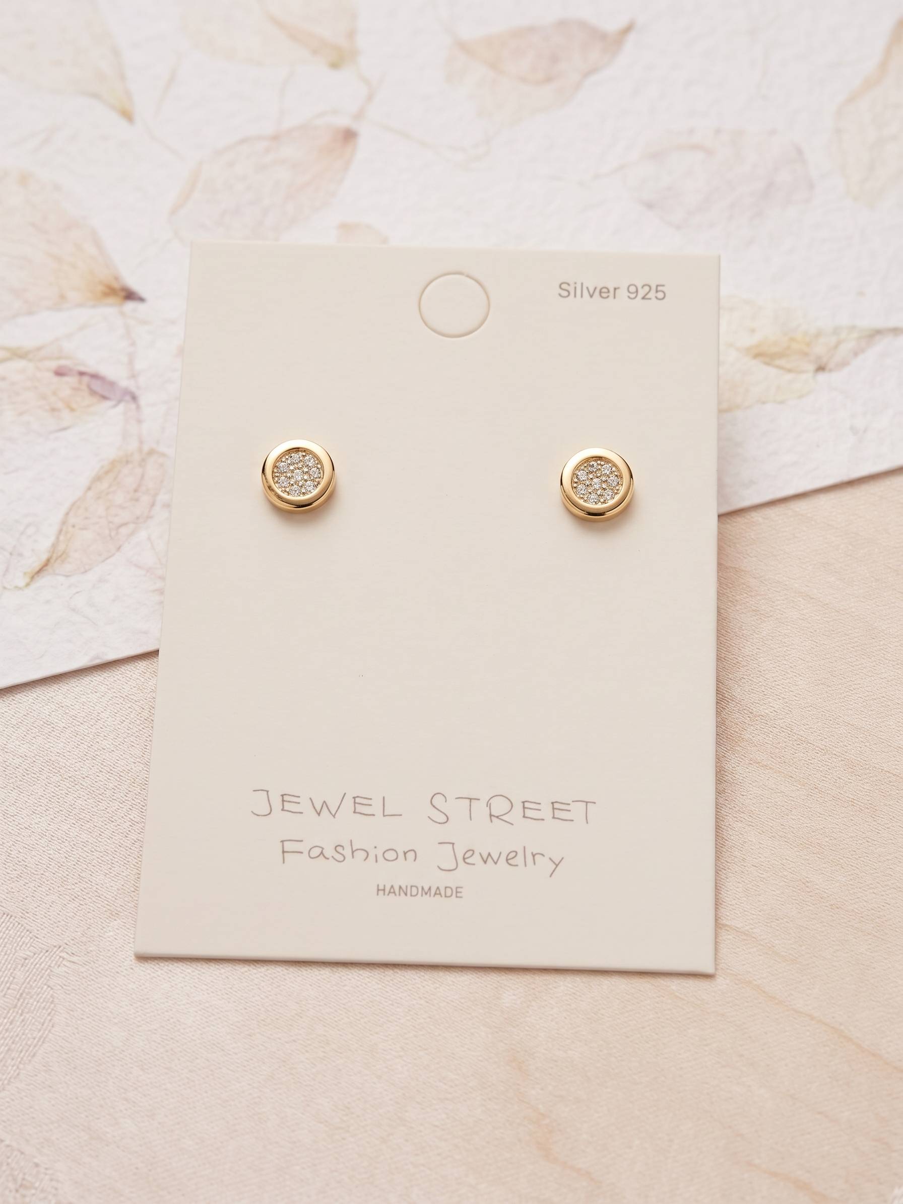 Gold earrings on a Jewel Street branded card with a floral background