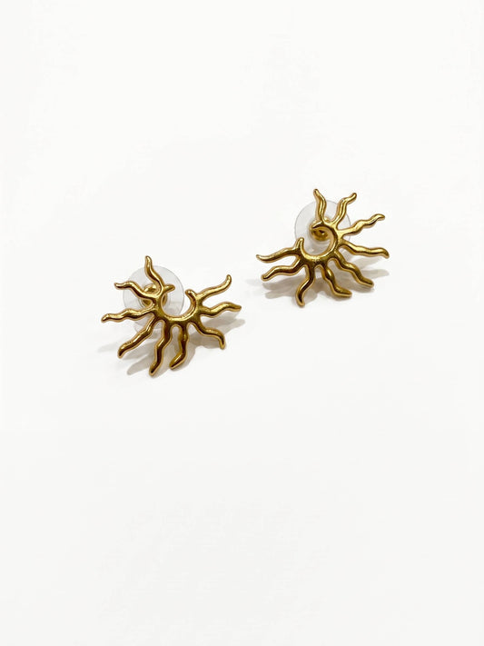 Gold sun-shaped earrings with a central gemstone on a white background