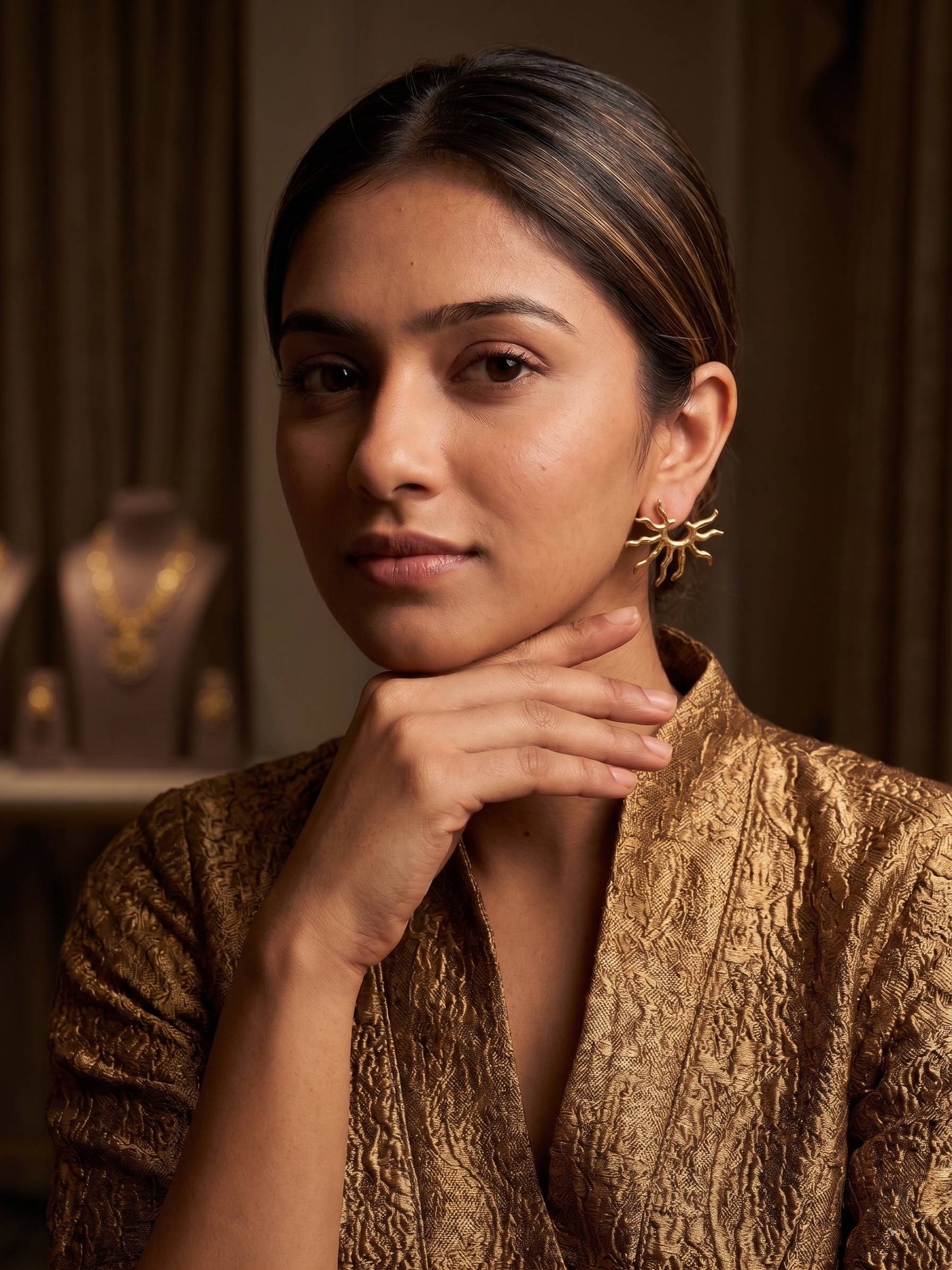 Gold sun-shaped earrings held in a hand against a white background