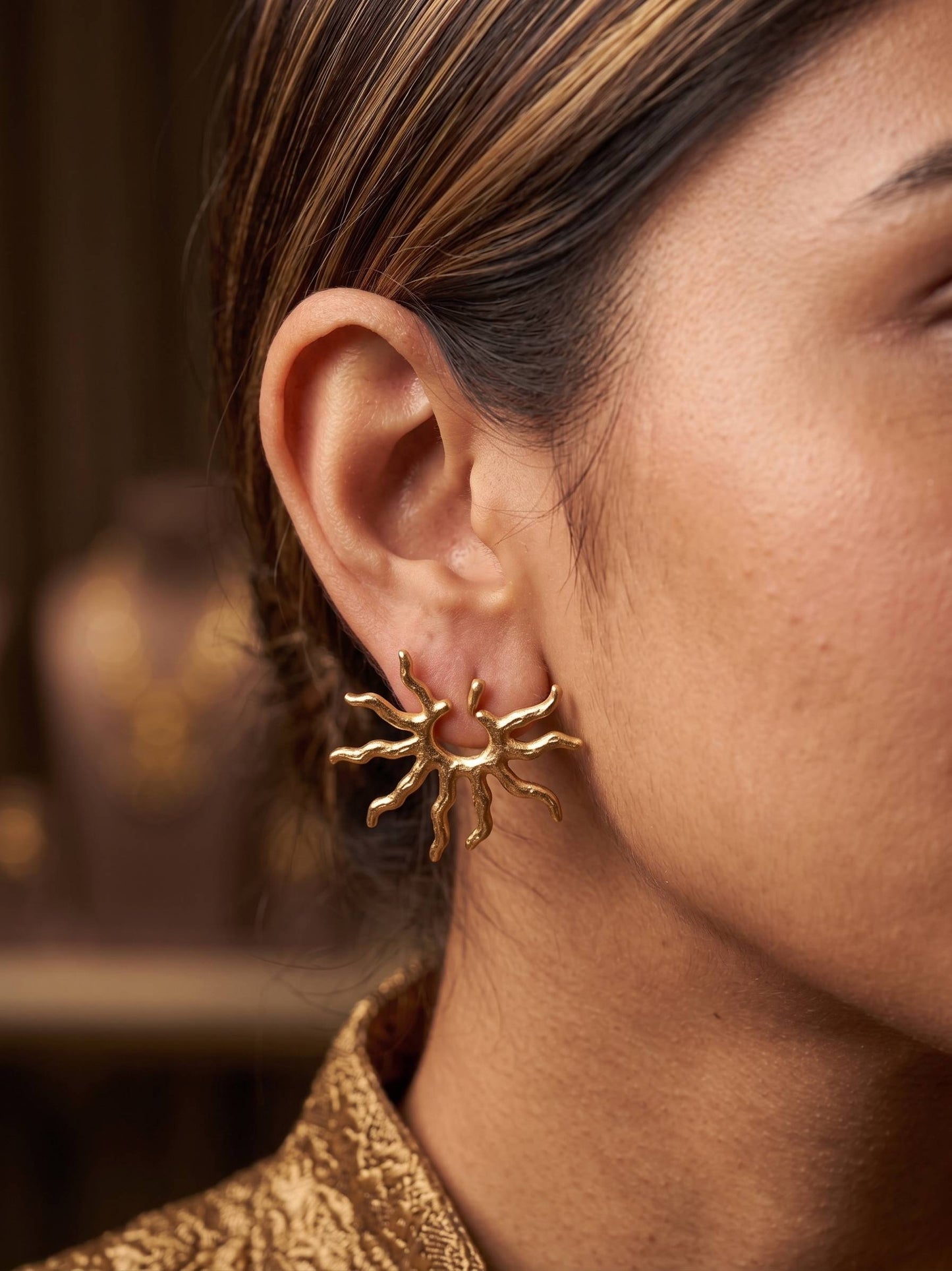 Gold sun-shaped earrings held in a hand against a white background