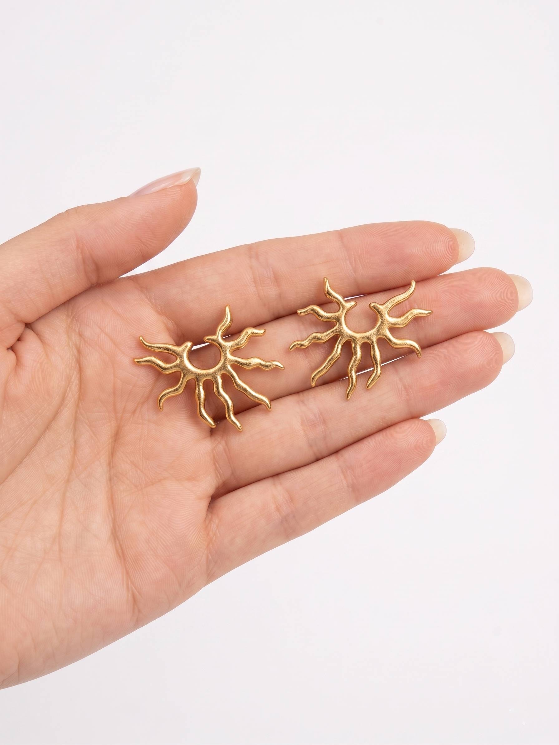 Gold sun-shaped earrings held in a hand against a white background