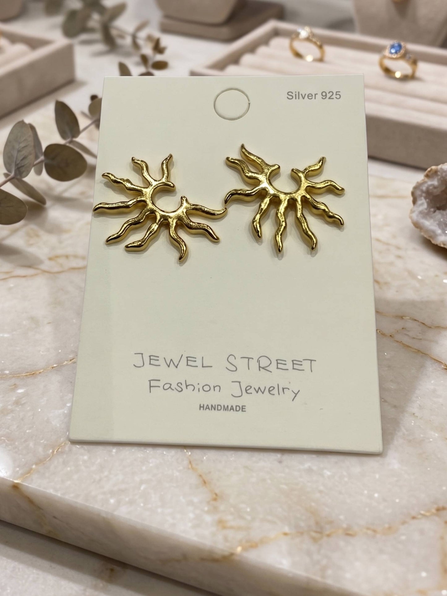 Gold sun-shaped earrings held in a hand against a white background