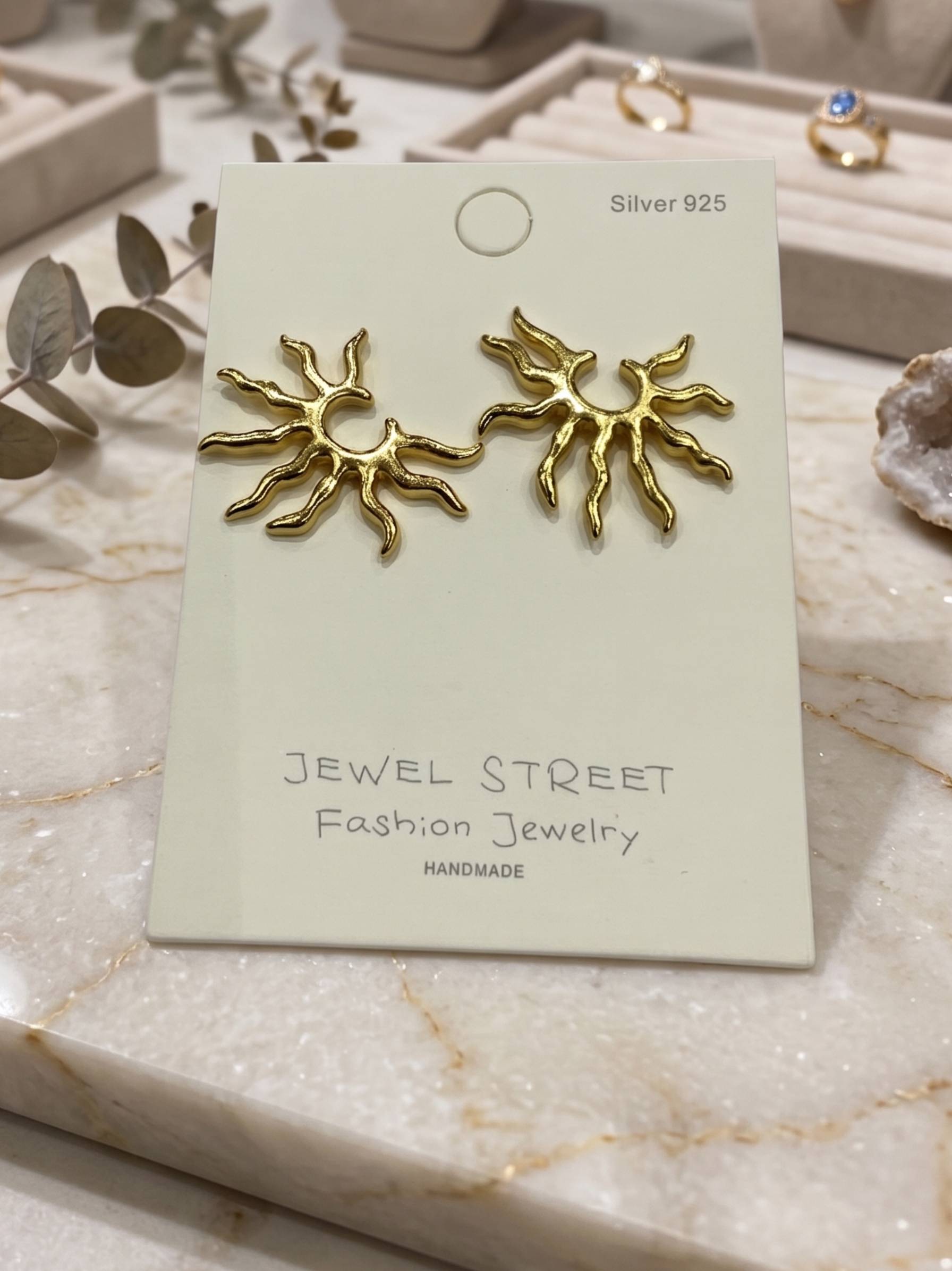 Gold sun-shaped earrings held in a hand against a white background