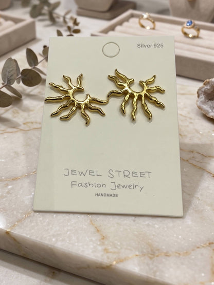 Gold sun-shaped earrings held in a hand against a white background