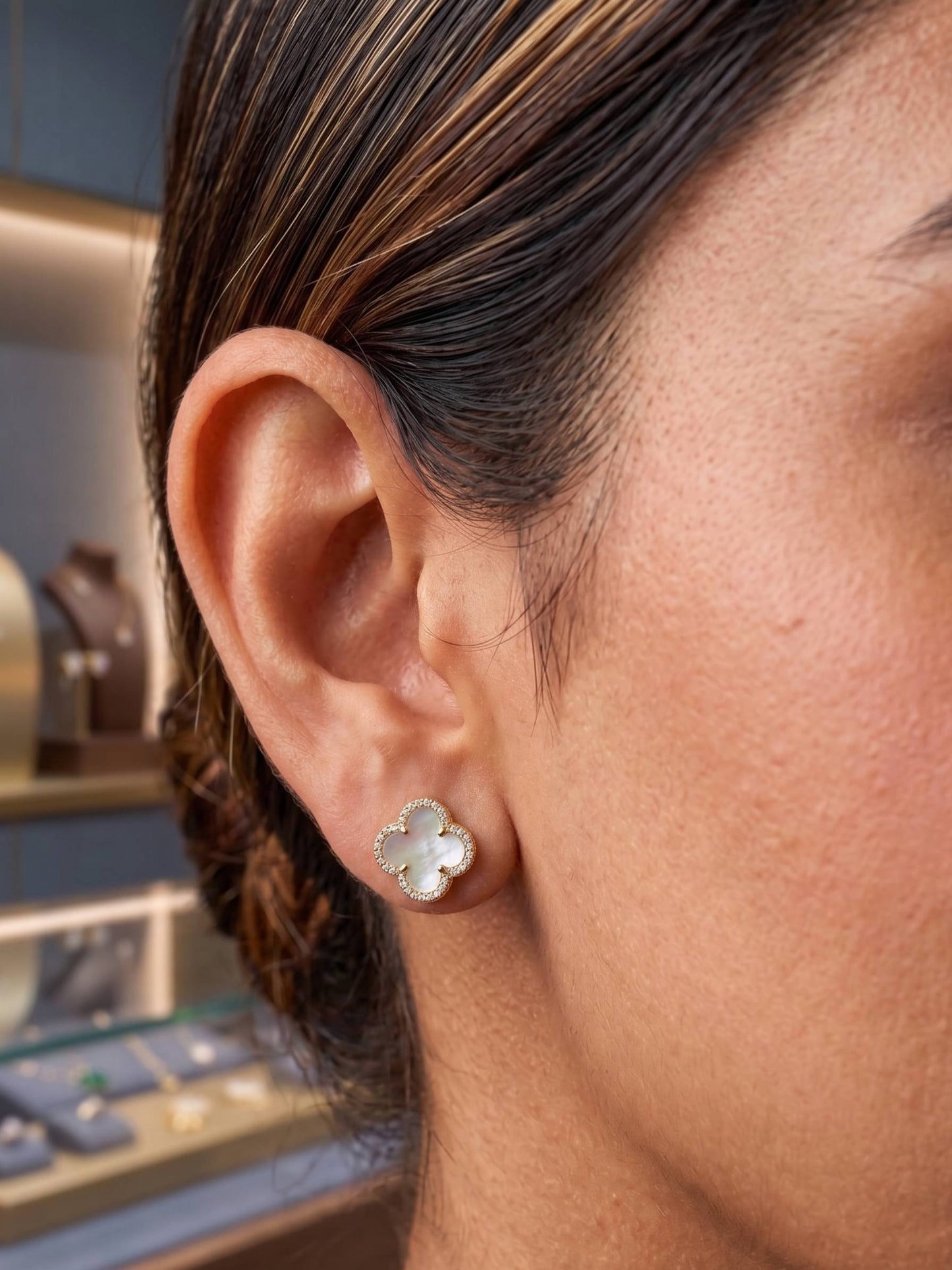 Close-up of a person wearing silver floral earrings with a jewelry store in the background.
