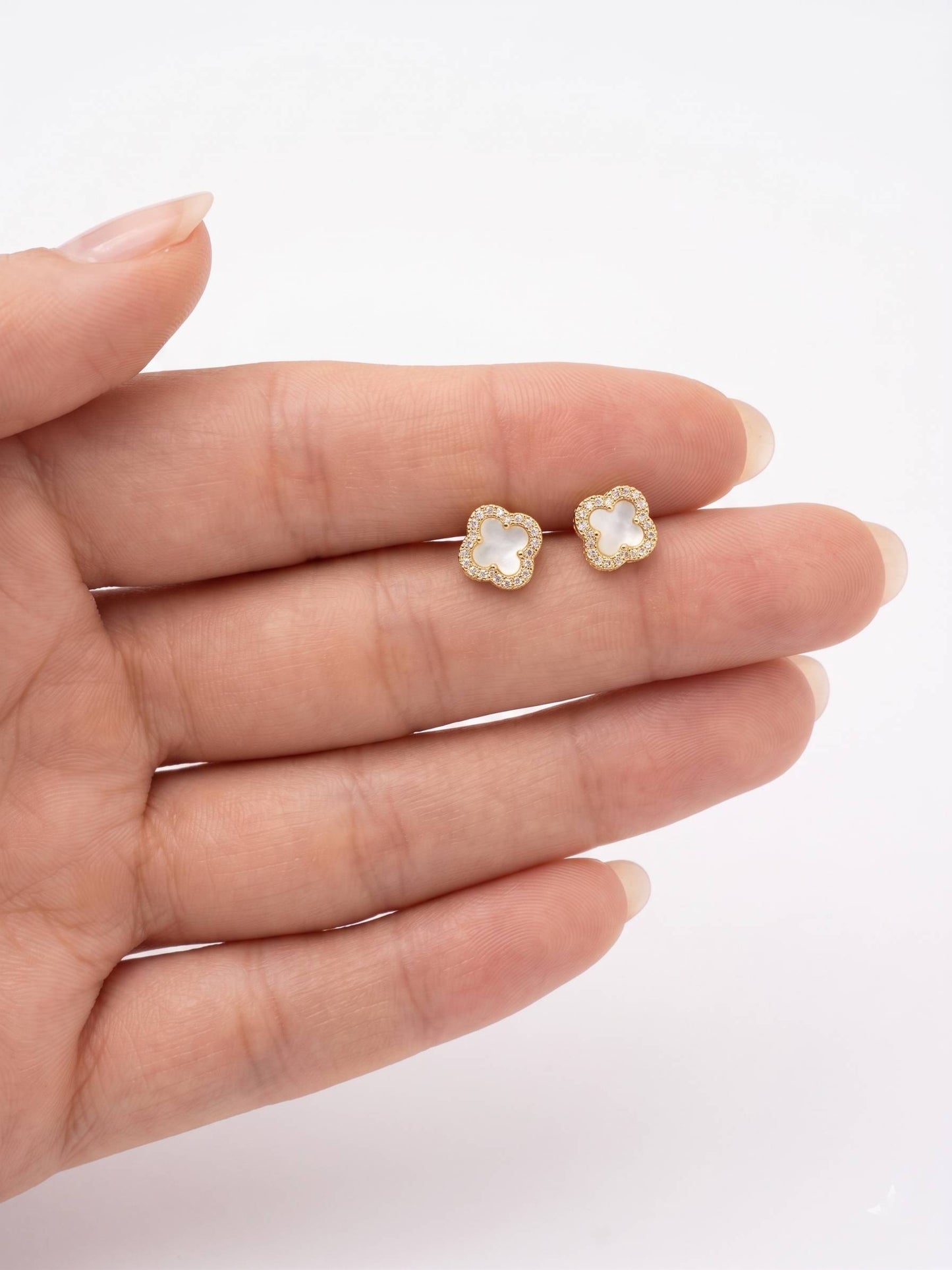Gold earrings with clear gemstones held between fingers on a white background