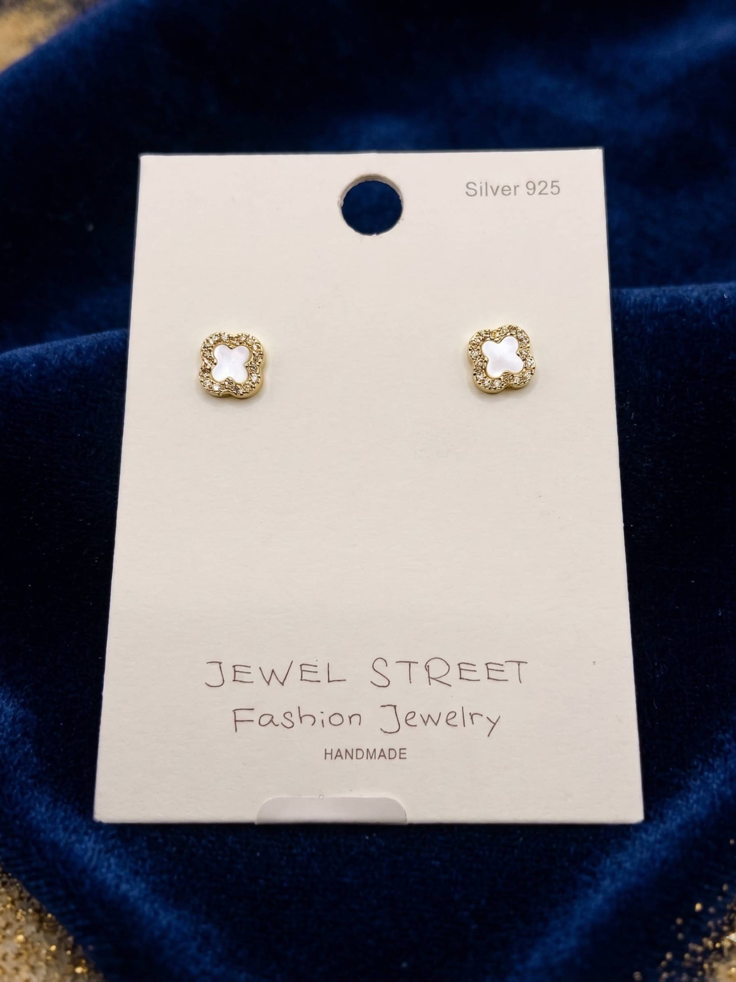 Gold earrings on a 'Jewel Street' branded card against a blue velvet background