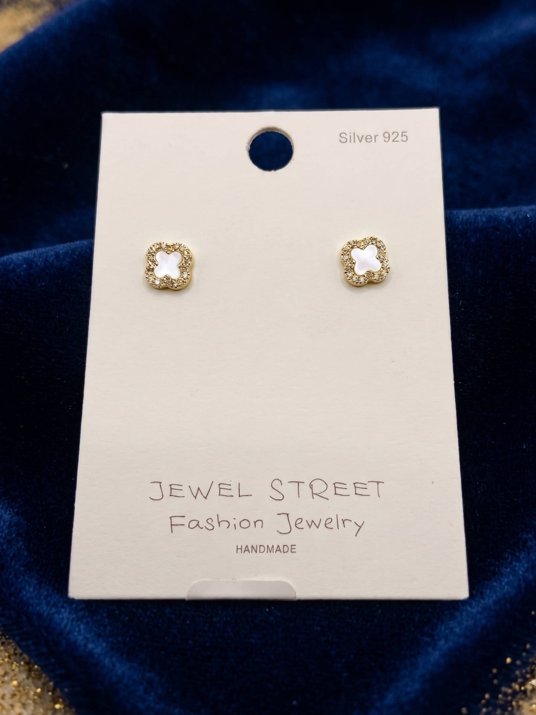 Gold earrings on a 'Jewel Street' branded card against a blue velvet background