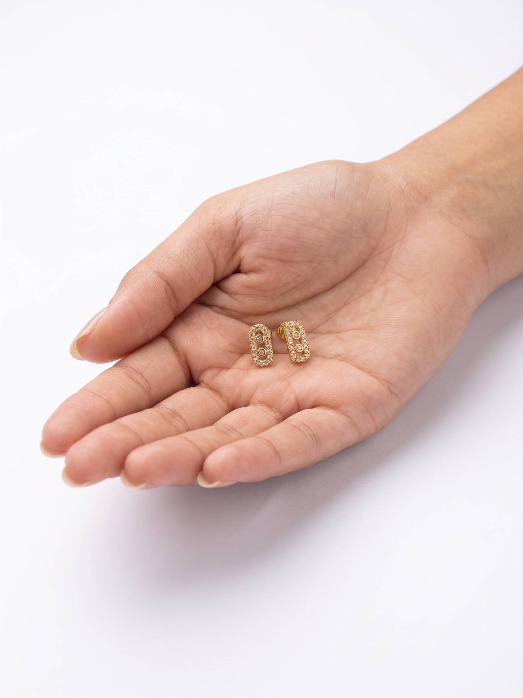 Gold earrings held in a hand on a white background