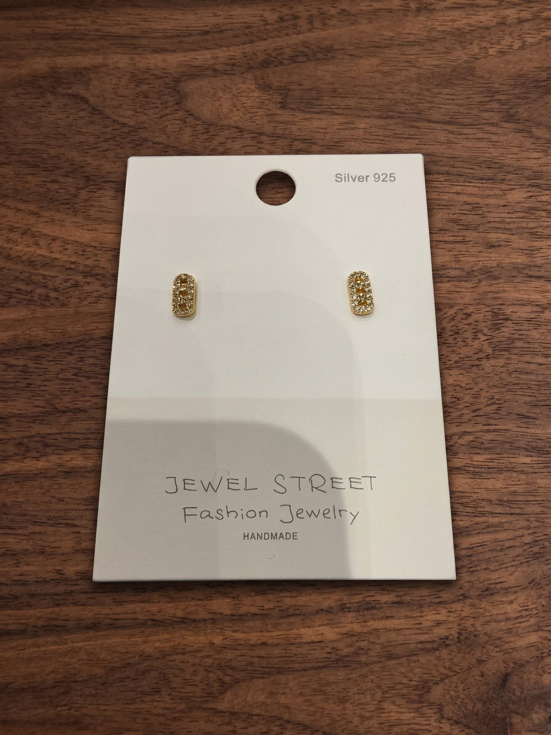 Gold earrings on a 'Jewel Street' branded card against a wooden background