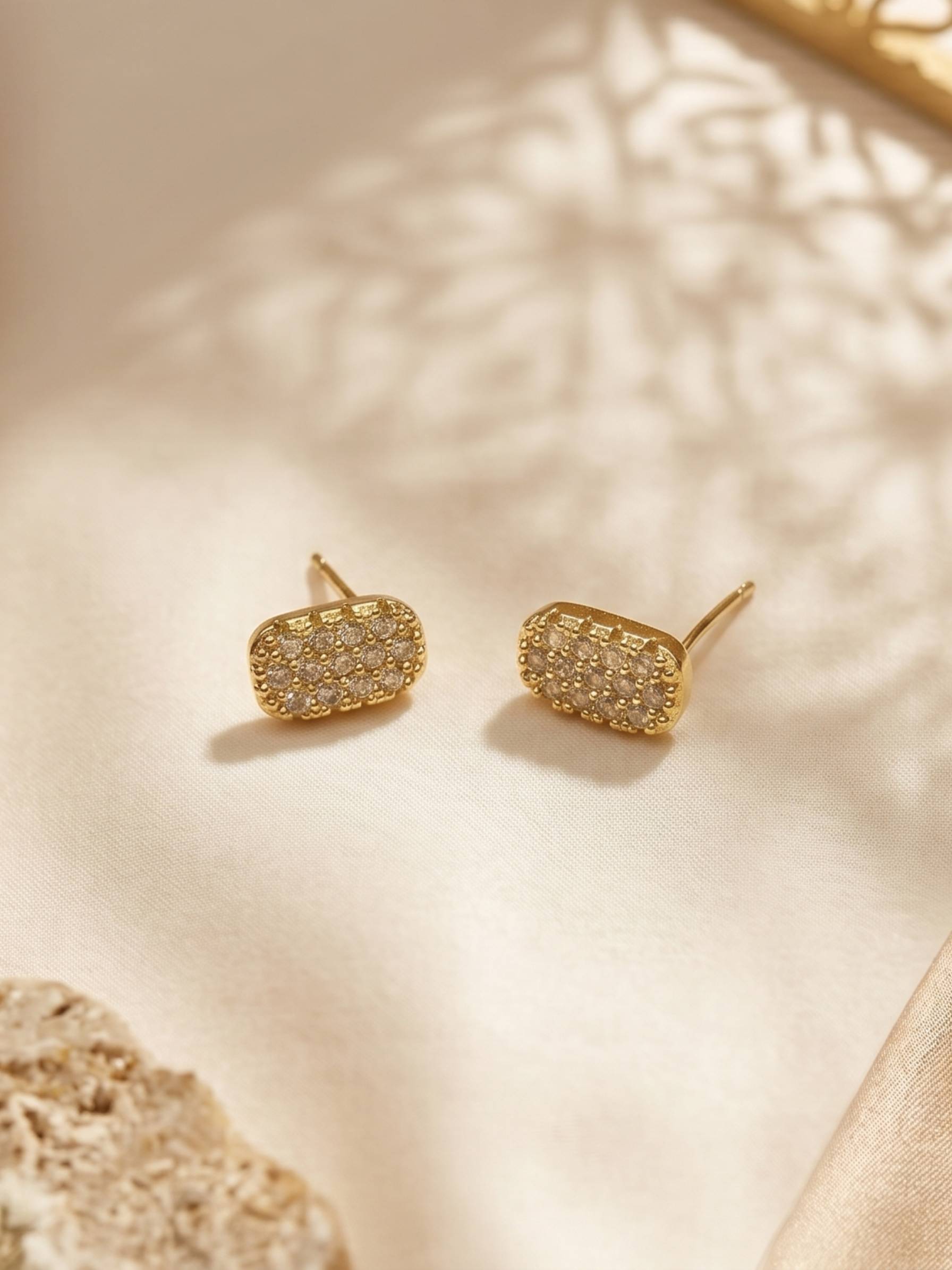 Gold earrings with a textured design on a beige surface